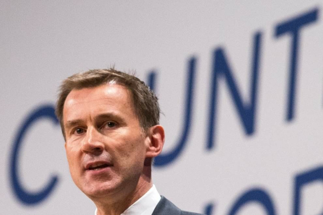 Jeremy Hunt standing in front of a backdrop with words on it. His head is in front of a letter so it says cunt behind his head