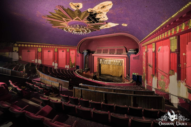 empty art deco cinema, in purple and red. there is a gold star bust from which hangs a chandelier