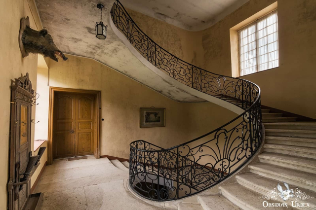 black metal spiral stairs in abandoned chateau. there is a taxidermy boars head on the wall
