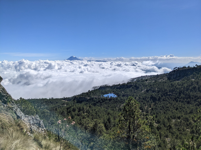 vista superior de la laguna desde una distancia de 400 metros. En el horizonte se levanta imponente el pico de Orizaba por sobre un mar de nubes que comienza no muy lejos de la laguna. El cielo, además del mar de nubes, no tiene ninguna otra.