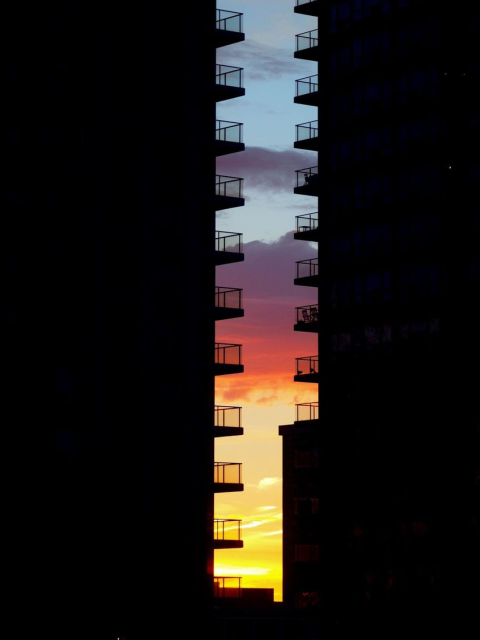 Sunrise or sunset photogrphed through a gap between two tall buildings. the buildings are completely dark and about 10 balconies are poking into the gap.