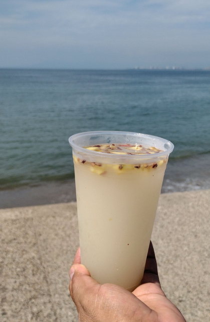 Mano sosteniendo vaso con licor bebida blanca frente al mar.