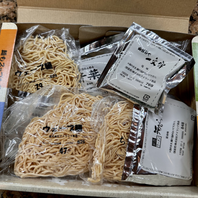 A box of four packs of noodles in packets, and four packs of soups