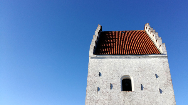 Looking up at a mass of lovely light summery blue cloudless sky that fills the frame. Off-centre, to the left, dominating the scene and the eye: the top of a rectangular old church tower. It is white stone, historically grubby and browning in patches. The triangular top is an eye-catching form – the edges rise in castellated edges – I don’t know what this is called technically, it reminds me of the spines on a dragon. Between them, startling against the blue sky and white stone, a slope of deep red roof tiles. In the centre of the white stone façade, some half-circular indentations – I won’t pretend I know what they are. In the very centre of them, a single window – a deep black opening right up at the top, where the belfry would be if there were a bell. You can’t see it from the photo, but this is the top of the Den Tilsandede Kirke – the Sand-Covered Church in Skagen on the tip of Denmark. It’s a 14th century Gothic church that slowly got covered by sand until it was abandoned in 1795, leaving just the top exposed ever since. All that history and weathering and architectural resilience and all the prayers and lives that have passed through it, now reduced by me to a social media post and I’m not even sorry, I’m just sharing in case anyone else likes the sight of it too.