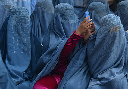 A line of women sit in Kabul, Afghanistan. They are all wearing traditional powder blue burkas. The woman in the centre is using a mobile phone to take a photograph. As she is holding up her hands, her burka is lifted to reveal a cerise pink silk tracksuit underneath. The difference between the two colours and tradition and modernity creates a striking image.
Photo by Shah Marai,  AFP Afghanistan