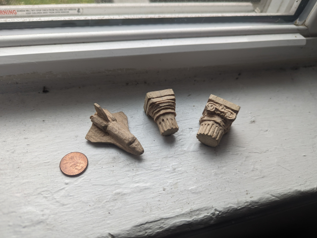 small basswood carvings of a space shuttle, a doric column capital and an ionic column capital next to a penny for scale