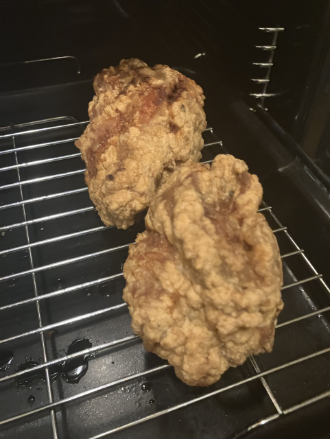 Two battered chicken thighs, resting on a cooling rack after the second round of deep frying, this time at 190C
