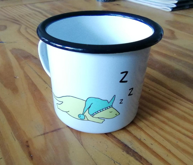 An enamel coffee mug with a sleeping dinosaur on one side.