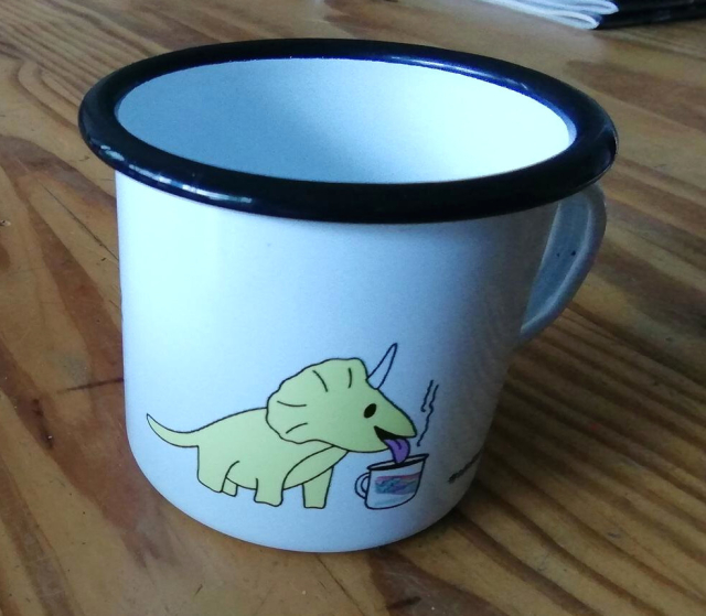 The same cup from the other side with the dinosaur awake and slurping coffee from a similar cup.