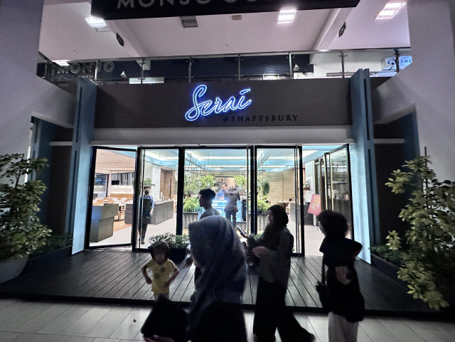 Entrance to 'Serai at Shaftsbury' restaurant with neon sign above the door, people walking by, and indoor seating visible through glass doors.