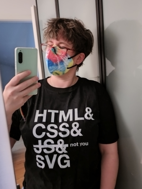 Mirror selfie of Sara, masked, wearing Heydon's
"HTML&
CSS&
(strikeout) JS& (end strikeout) not you
SVG"
T-shirt.
