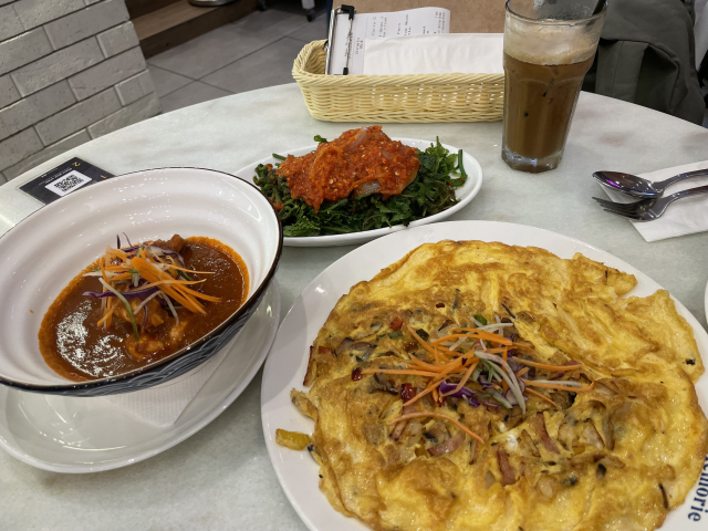 A bowl of chicken cooked in a very red curry, a large plate of mushroom omelette, and a plate of green blanched fern fiddleheads mixed with a fiery chili sambal. 
