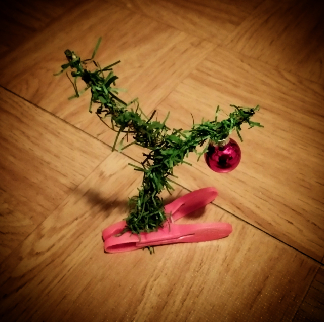 Photo. A color photo of a homemade Christmas tree made from a red clothespin, a sprig of forked plastic fir greenery and a red mini Christmas tree ball. It's not meant seriously. It really is very ugly.