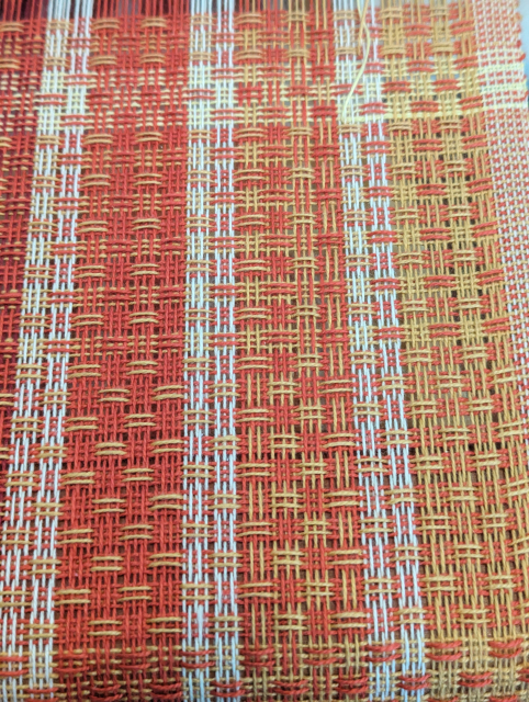 close up of huck lace cloth on the loom, in orange and yellow and white yarns