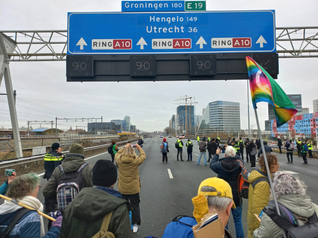 Some Extinction Rebellion members blocking the A10 highway in Amsterdam with lots of police vans in the distance