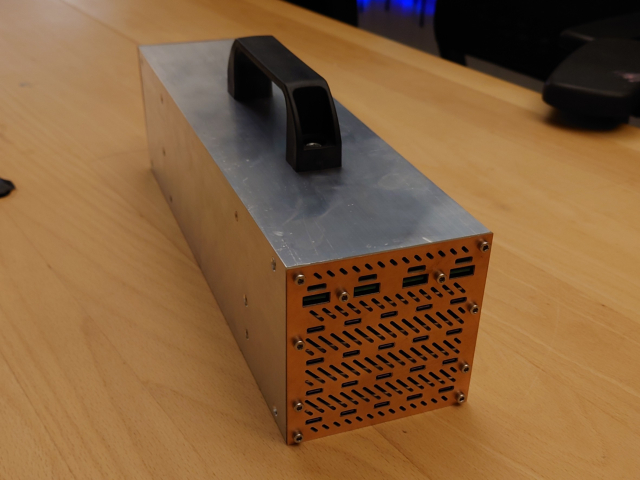 Front view of the finished #PDBrick prototype.
The 24 USB-C ports are prominently visible in cutouts in the raw copper PCB front.
A black plastic handle is mounted on top of the aluminum extrusion.