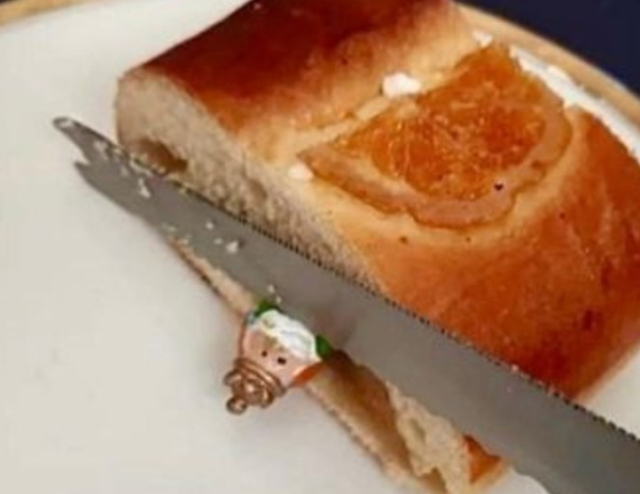 Porción de roscón de reyes en la que asoma la cabeza de la figura del rey y el cuchillo de cortar el roscón sobre su cuello