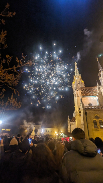 People in a square in front of a stone cathedral watch fireworks.