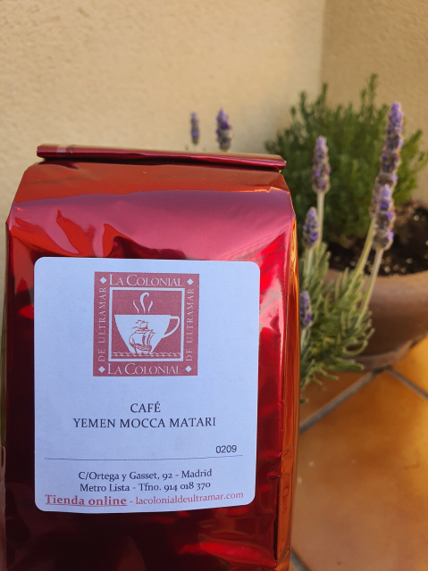 Glossy dark red bag bearing the label Café Yemen Mocca Matari. In background: lavender plant in bloom.