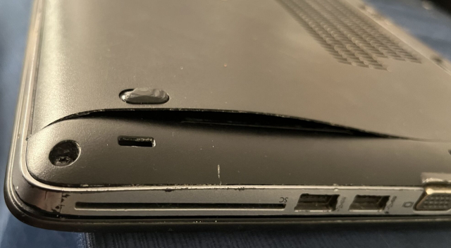 An upside-down worn-out HP Elitebook 840 G1. The bottom cover is bent, arcing up and exposing the inside like a bent sheet of paper.
