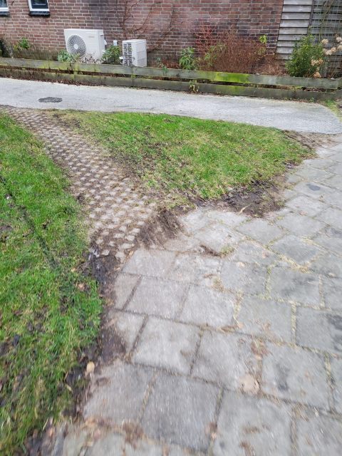 Desire path paved with grass pavers cutting off very sharp corner in footway, surrounded by bicycle tire tracks.