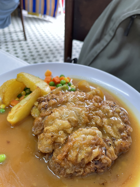 A plate of food with battered meat covered in gravy, accompanied by fries and mixed vegetables (peas and carrots).