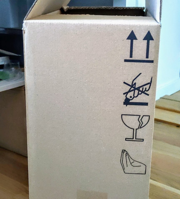 A box with various symbols like "keep it up", "do not open with a cutter" and an "Italian hand gesture".