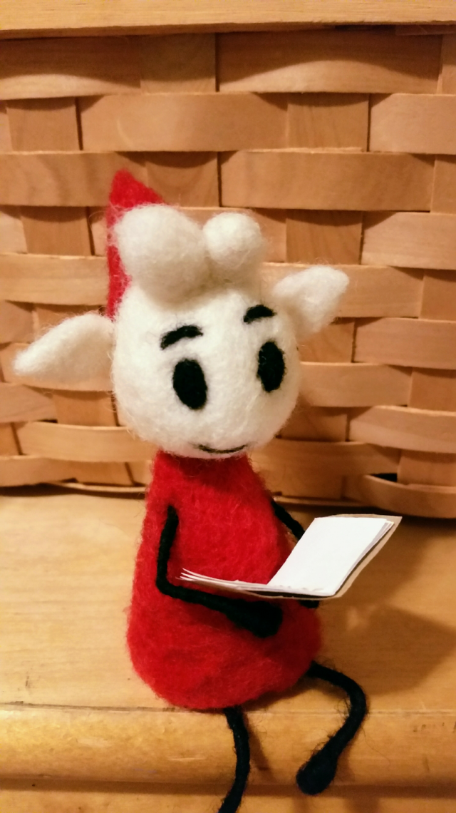 Needle felted Alfur sitting in front of a basket reading a report.