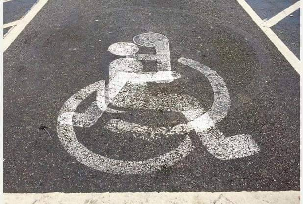 A parking spot has two painted versions of the International Symbol of Access. It is done in such a way to look like the two are cuddles and kissing.