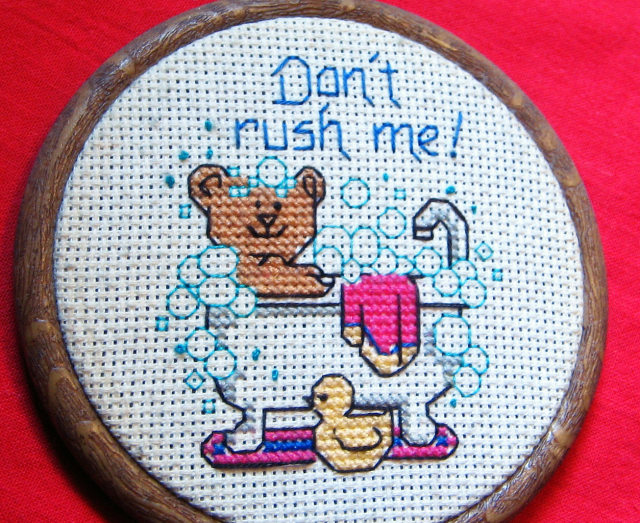 A piece of crosstitching work with a bear in a bathtub and rubber ducky, with the message, Don't rush me!