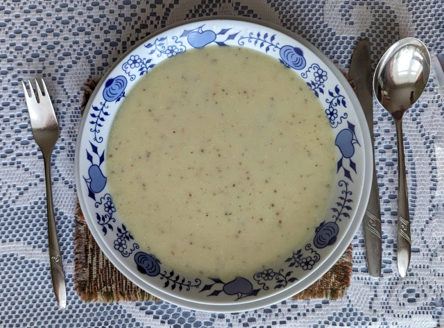 Talíř obsahující nažloutlou polévku s tmavými zrníčky hořčice.