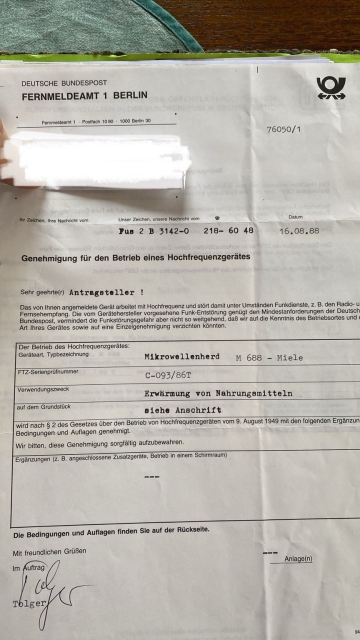 A crumpled document from the Deutsche Bundespost Fernmeldeamt 1 Berlin, dated 1988, regarding the approval for the operation of a high-frequency device (microwave oven). Some personal information is redacted.
Text from image:

Genehmigung für den Betrieb eines Hochfrequenzgerätes
Der Betrieb des Hochfrequenzgerates:
Geräteart, Typbezeichnung
Mikrowellenherd M 688 - Miele
FTZ-Serienprüfnummer
C-093/ 86T
Verwendungszweck
Erwärmung von Nahrungsmitteln
auf dem Grundstück
81ehe Anachrift
Bedingungen und Auflagen genehmigt.
Wir bitten, diese Genehmigung sorgfältig aufzubewahren.
wird nach § 2 des Gesetzes über den Betrieb von Hochfrequenzgeräten vom 9. August 1949 mit den folgenden Ergänzun
Sehr geehrte(r) Antragsteller !
Das von Ihnen angemeldete Gerät arbeitet mit Hochfrequenz und stört damit unter Umständen Funkdienste, z. B. den Radio- u Fernsehempfang. Die vom Gerätehersteller vorgesehene Funk-Entstörung genügt den Mindestanforderungen der Deutsch Bundespost, vermindert die Funkstörungsgefahr aber nicht so weitgehend, daß wir auf die Kenntnis des Betriebsortes und Art Ihres Gerätes sowie auf eine Einzelgenehmigung verzichten könnten.
Ergänzungen (z. B. angeschlossene Zusatzgeräte, Betrieb in einem Schirmraum)
