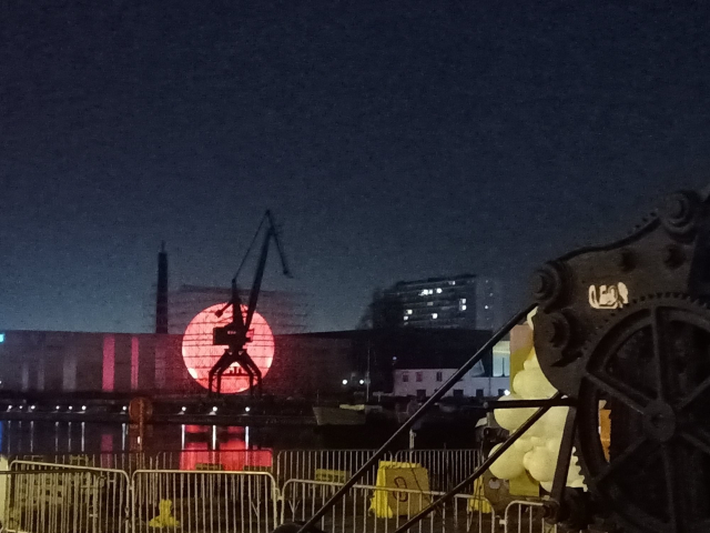 The silhouette of an old crane against a big, red, glowing spherr