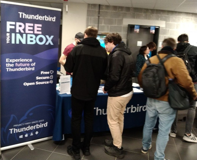 Le stand de Thunderbird au Fosdem 2024 avec un poster sur fond bleu mentionnant : Thunderbird / Free your inbox / Experience the future of Thunderbird / Free / Secure / Open Source / Privacy first since 2003 / Thunderbird (@Hellosct1@mamot.fr, recadrée)