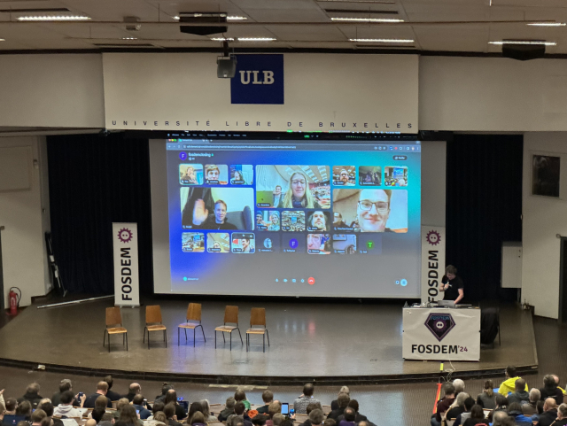 A screenshot of the Janson stage with Matthew speaking, and Element Call with many attendees projected on the screen