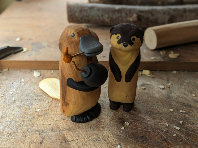 Wood sculpture of a platypus holding a bomb ready to light the fuse and a standing otter