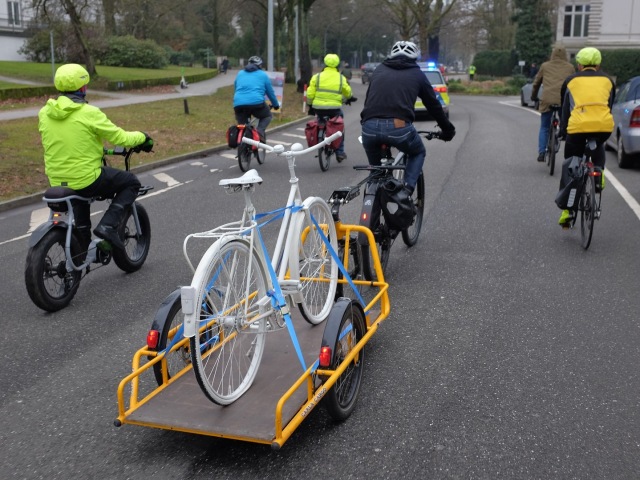 Ride of Silence mit mehreren Teilnehmern; ein Fahrrad zieht einen Anhänger, der ein Ghostbike transportiert