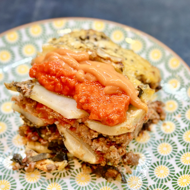 Homemade moussaka on a colorful dish. Shows a cross section of eggplants, potato and sauce 