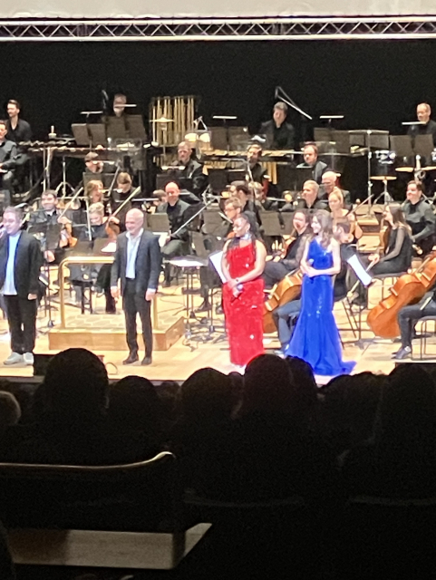 J'Nique Nicole in a red dress, and Emi Evans in a blue dress, on stage