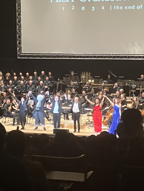Yoko Taro, Yosuke Saito, J'Nique Nicole, and Emi Evans holding hands on stage for the NieR Orchestra Concert in London