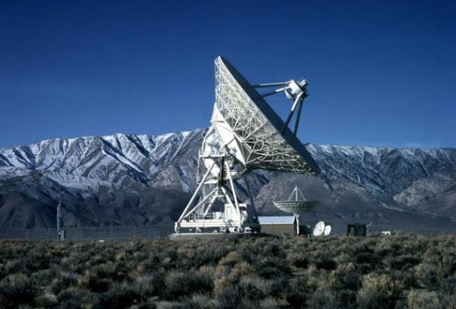 A single radio telescope in front of a backdrop of snow-capped mountains. It is one of the ten 25 metre dishes scattered around the United States that make up the Very long Baseline Array (VLBA).