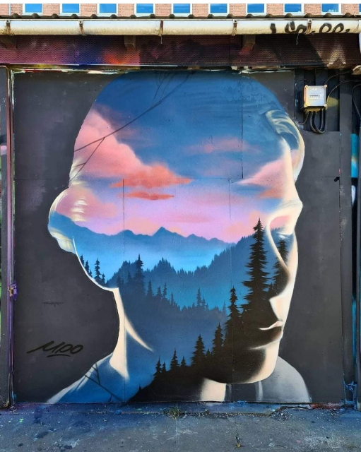 Streetartwall. The mural of a female silhouette was sprayed/painted on a long street art wall in the backyard of a concert hall. The background is black. In pastel colors, instead of a face, a landscape with hills full of pine forests can be seen under a pink-blue sky. A beautiful, dreamy mural that unfortunately may not have existed for long due to its public graffiti location.