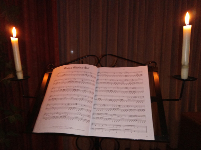 A relatively dark room. A music stand in it, with an open music book. The stand has a candle at each of the two sides, illuminating the pages.