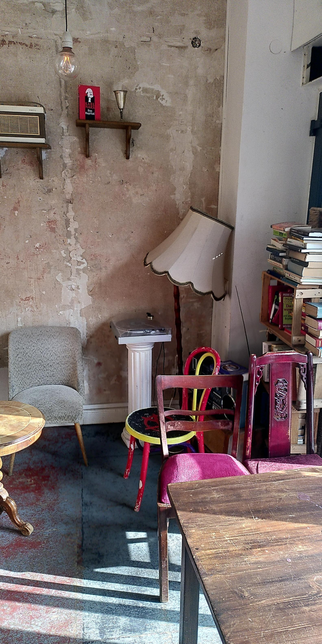 A portrait picture of the corner of the cafe.

There is a red book on display on the wall "Das Kapital"

And a a bunch of books stacked. 

There is also chairs, tables and a broken large lamp.