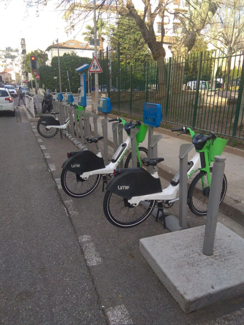 Une borne de vélo bleu (vélo de location de la ville de Nice) désaffectée sur laquelle sont posés des ebikes de la société Lime mon cul