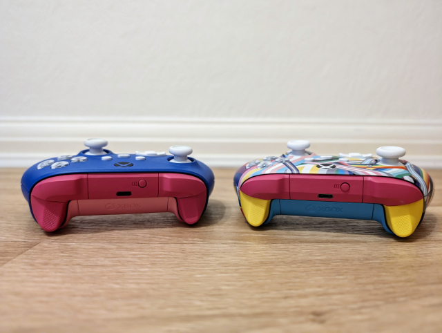 Two Xbox controllers with their backside towards the camera.

The left one has a blue top plate, dark pink shoulder buttons and trigger buttons, and a pink underside; resembling a bi pride flag.

The right controller has a top plate with dozens and dozens of different pride flags, pink shoulder buttons, yellow trigger buttons, and a light pink underside; resembling a pan pride flag.