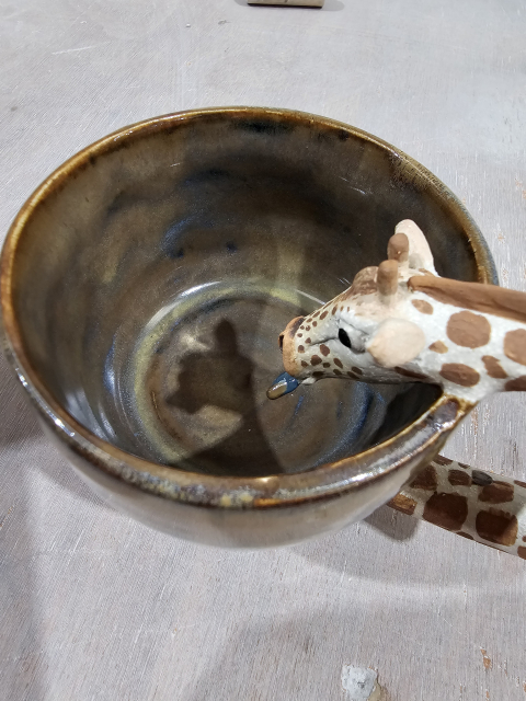 Shadow of giraffes head inside the mug, mug is brown ish with blue and green flecks