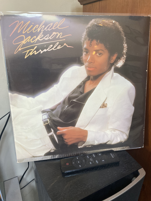Vinyl record cover for "Michael Jackson Thriller" resting on a surface with a television remote in front.