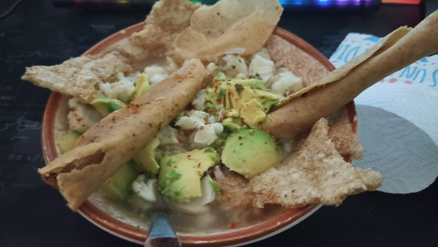 Foto de un plato de pozole blanco estilo Guerrero, lleva chicharrón, tostadas y tacos dorados, aguacate, epazote y chile en polvo