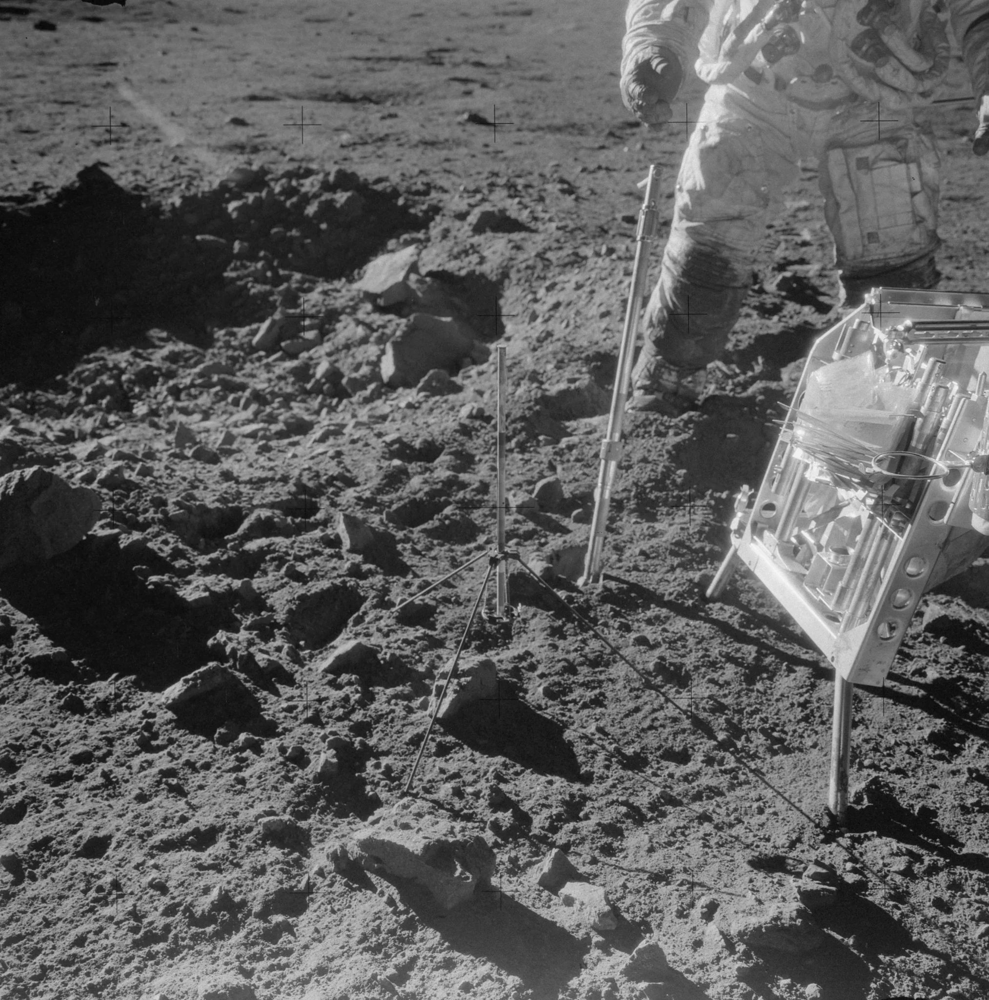 An astronaut stands on lunar soil to the right of frame, tending to surface experiments filled with tubing and wires. The boots of their spacesuit are deeply blackened from a coating of lunar dust. https://www.nasa.gov/history/alsj/picture.html